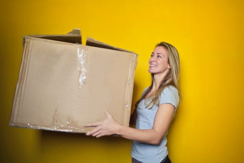 Lady smiling holding a large packaging box set with a yellow background